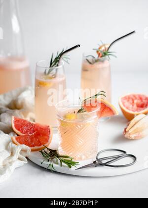3 bicchieri di cocktail di pompelmo su vassoio di marmo con fette di rosmarino e pompelmo Foto Stock