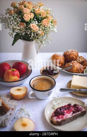 Pane con burro e marmellata, croissant, mele e caffè serviti per colazione su tovaglia di lino bianco Foto Stock