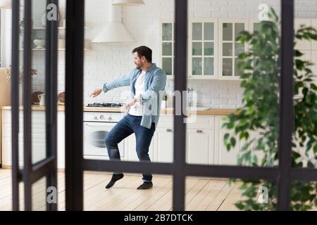 Divertente uomo positivo ballare in cucina moderna da solo Foto Stock