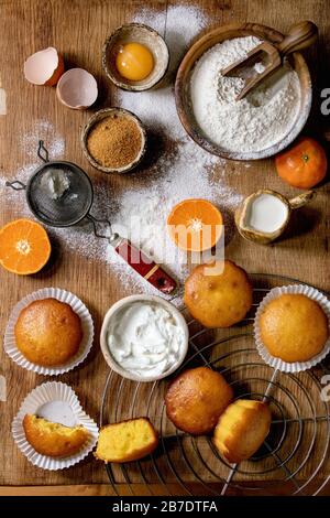 Arance di agrumi o clementine fatte in casa dolci muffin con farina e ingredienti sopra il legno tagliere come sfondo. Disposizione piatta, spazio Foto Stock