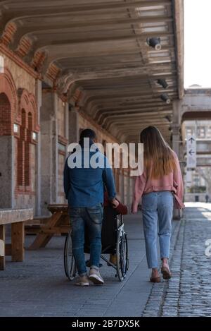 Un giovane latino-americano paralizzato in carrozzina accompagnato da una giovane ragazza caucasica e latino-americana che passeggiando felicemente per la strada Foto Stock