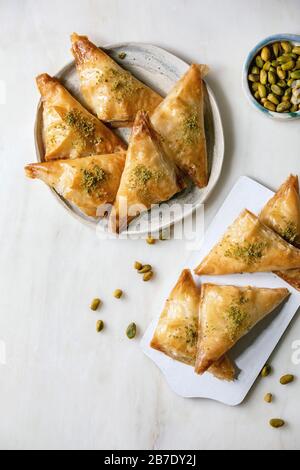 Tradizionale dolce turco fatto in casa baklava con pistacchio servito su tagliere di legno bianco con ciotola di noci su sfondo di marmo bianco. Piatto Foto Stock