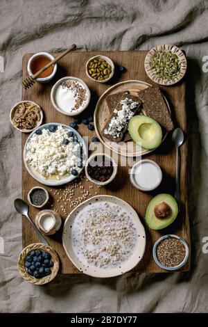 Colazione sana. Varietà di piatti per la colazione: Grano, yogurt, kefir, formaggio fresco, avocado, pane di segale, semi, frutta secca e bacche assortite in ceramica Foto Stock