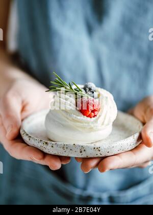 Piatto da donna con mini Pavlova torta decorata con frutti di bosco freschi e rosmarino. Composizione verticale. Spazio copia superiore. Foto Stock