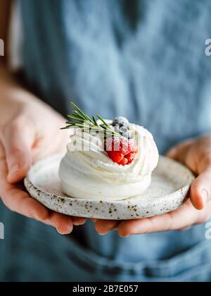 Piatto da donna con mini Pavlova torta decorata con frutti di bosco freschi e rosmarino. Composizione verticale. Spazio copia superiore. Foto Stock