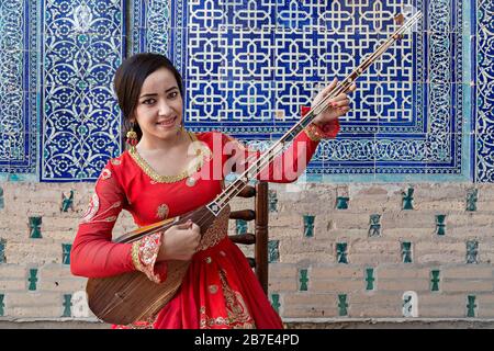 Donna uzbeka in costume nazionale che gioca strumento musicale locale del Dutar, a Khiva, Uzbekistan Foto Stock