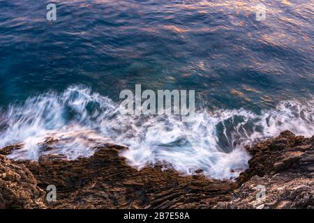Onde che si schiacciano sulle scogliere come visto dall'alto durante il tramonto Foto Stock