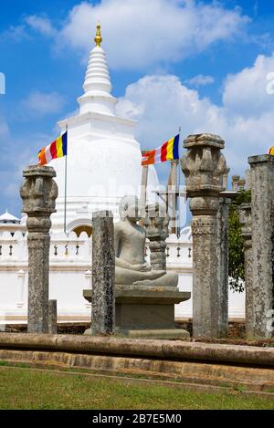 Scultura di un Buddha seduto sulle rovine di un antico tempio sullo sfondo di Dagoba Tuparam. Anuradhapura, Sri Lanka Foto Stock