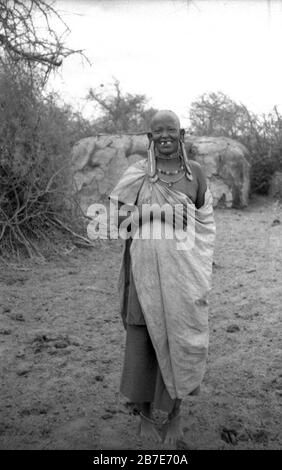 Anni '60, storico, fuori nel cespuglio africano, una donna Maasai sorridente in abiti tradizionali. Un gruppo di persone nilotiche, il Masssai livie uno stile di vita semi-nomade e parlare la langage Maa. Abitano la regione dei grandi laghi africani. Foto Stock