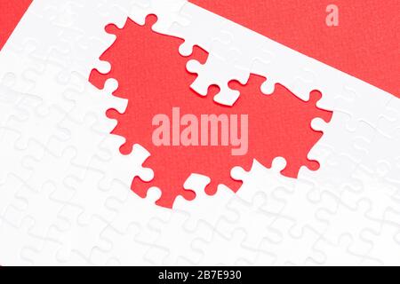 Cuore da puzzle bianchi come simbolo di amore su uno sfondo rosso. I fan gradiscono puzzle che si completano a vicenda Foto Stock