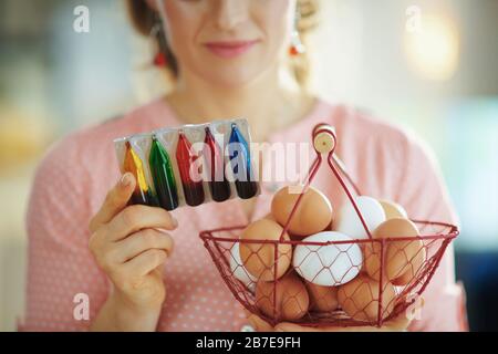 Primo piano su donna che tiene il cesto con le uova e le istruzioni di lettura sul pacchetto di colorazione alimentare nel soggiorno in sole primavera giorno. Foto Stock