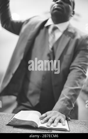 Colpo in scala di grigi di un maschio afroamericano che prega con la mano Sulla Bibbia Foto Stock