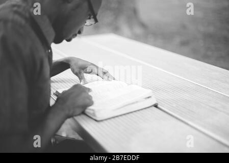 Immagine in scala di grigi di un maschio afroamericano seduto a un tavolo E leggendo la Bibbia Foto Stock
