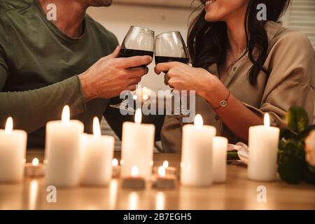 Immagine di una felice coppia appassionata che beve vino rosso dai bicchieri mentre si ha una romantica cena a lume di candela a casa Foto Stock