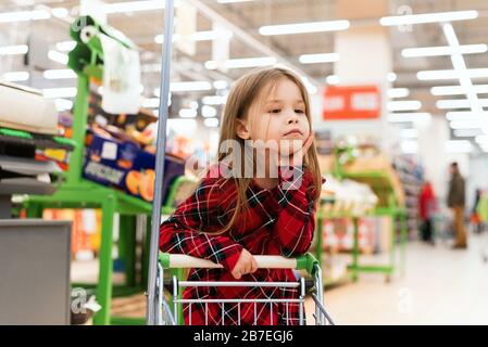 Un bambino triste si alza dietro il carrello e seleziona i prodotti a casa. Scaffali vuoti nei negozi, pandemia e isteria a causa di coronavirus. Foto Stock