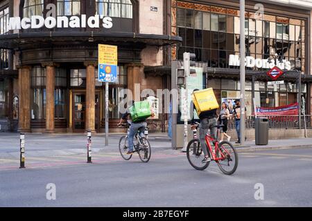 Un Uber mangia e un giro in ciclista di delivery glovo attraverso la Gran Via, Madrid, passando i pochi pedoni durante lo Stato di emergenza per il virus Corona Foto Stock