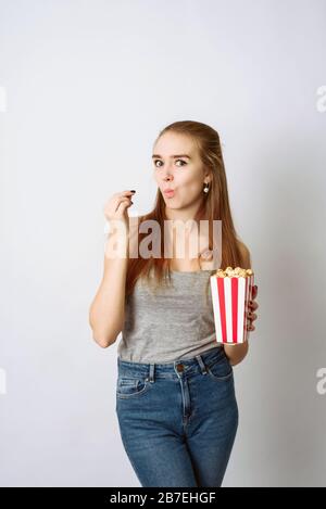 Bella ragazza bionda mangiare popcorn e guardare comedia film isolato su sfondo bianco. Copy Space, modello per blog e pubblicità. Donna tenere pop corn e guardare in macchina fotografica. Foto Stock