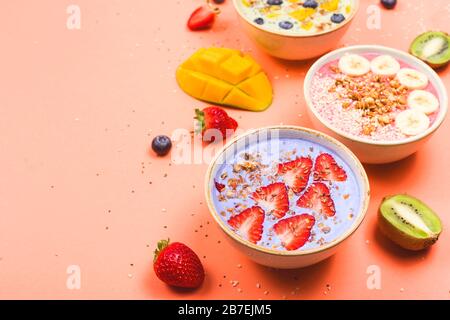 Bellissime ciotole multicolore per frullati salutari con frutti di bosco e supercibi su uno sfondo luminoso. Cibo estivo per il concetto di detox. Sfondo con copyspace. Foto Stock