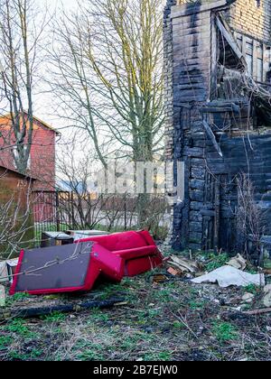 vecchia casa di legno dopo il fuoco, divani rossi vicino alla casa Foto Stock