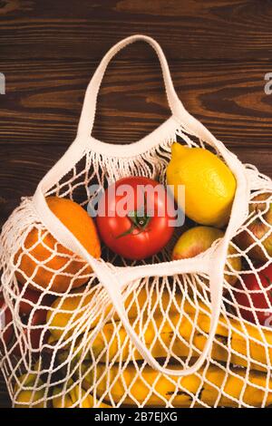 Borsa a corda riutilizzabile in cotone piena di verdure e frutta su un tavolo in legno. Concetto di stile di vita senza sprechi. Foto Stock