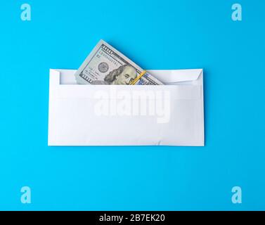 confezione di carta americana cento dollari fatture legate con una fascia elastica e si trova in una busta bianca su uno sfondo blu, il concetto di una tangente, Inves Foto Stock