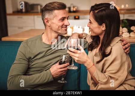 Immagine di una felice coppia appassionata che beve vino rosso dai bicchieri mentre si ha una romantica cena a lume di candela a casa Foto Stock