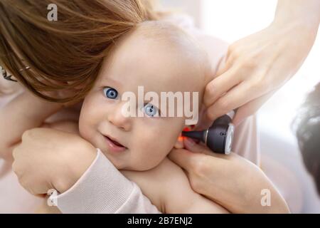 Dottore pediatra che esamina l'orecchio dei bambini con otoscopio. Mamma che tiene il bambino con le mani. Medicina, sanità, pediatria e persone. Assistenza ai bambini e. Foto Stock