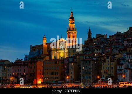 Vista serale sulle case e la basilica illuminata di Saint Michel Archange nella città vecchia di Menton, Francia. Foto Stock