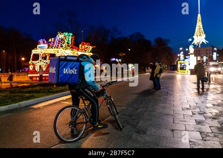 Varsavia, Polonia - 20 dicembre 2019: Wolt corriere in abiti da lavoro blu consegna uomo che consegna online cibo ordini in bicicletta in inverno di notte con pe Foto Stock