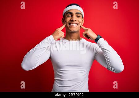 Giovane sportivo afro-americano che indossa abbigliamento sportivo su sfondo rosso Sorridente con bocca aperta, dita che puntano e costringono sorriso allegro Foto Stock