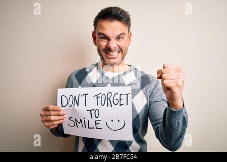 Giovane bell'uomo che tiene bandiera con il messaggio positivo divertente su sfondo bianco infastidito e frustrato urlando con rabbia, pazzo e urlando con Foto Stock