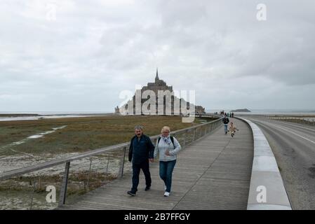 Turisti che camminano sul ponte di legno passerella accesso a Mont Saint-Michel, Normandia, Francia, Europa Foto Stock