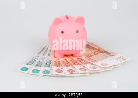 Scatola di moneta rosa piggy su mucchio delle banconote rubli russe su sfondo grigio, concetto di valuta Foto Stock