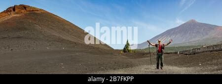 Viaggiatore con bastone da trekking e macchina fotografica vicino al vulcano Arenas Negras e campi di lava intorno. Cielo blu brillante e nuvole bianche. Parco Nazionale del Teide w Foto Stock