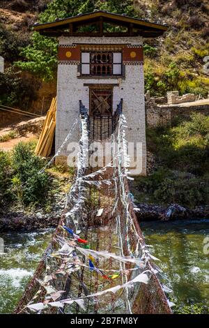 Ponte sospeso della catena del ferro di Tachog Lhakhang del XV secolo attraverso il fiume Paro Chu in Bhutan in una giornata di sole Foto Stock