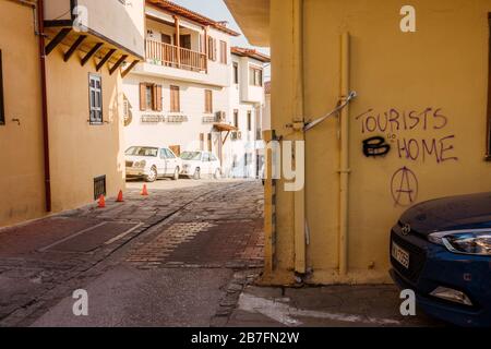 'I turisti vanno a casa' è cambiato in 'turisti B casa' - anti-turismo ha trasformato graffiti pro-turismo su un muro a Salonicco, Grecia Foto Stock