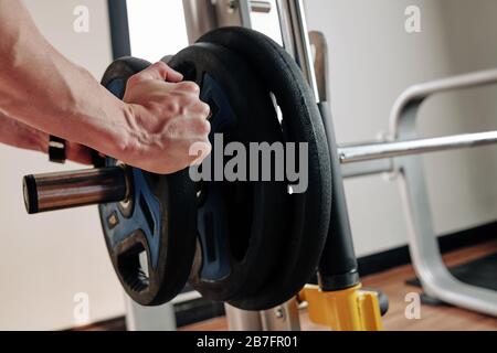 Immagine ravvicinata di un sportivo che mette pesanti piastre di peso sul barbell prima di allenarsi in palestra Foto Stock