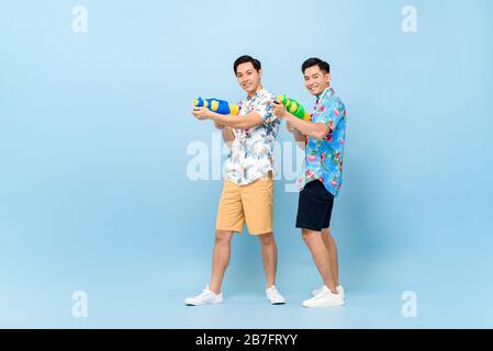 Smilng felici amici asiatici maschi che giocano con cannoni ad acqua in background isolato blu per il festival Songkran in Thailandia e nel sud-est asiatico Foto Stock