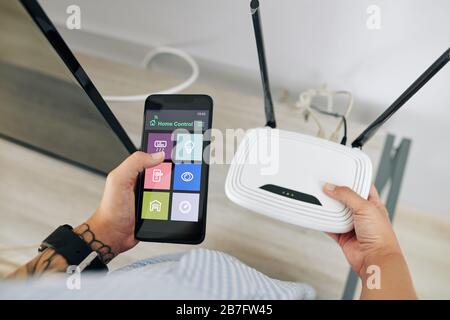 Mani di donna che accende il router wi-fi con l'applicazione smart home sul suo telefono Foto Stock