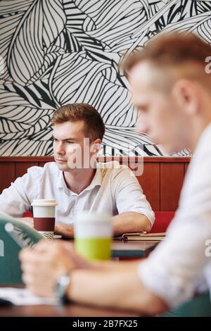 Un giovane uomo d'affari che lavora su un computer portatile al bar locale e beve una tazza di caffè Foto Stock