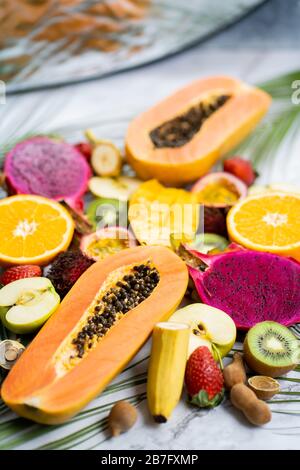 Assortimento di diversi frutti esotici a fette con foglie tropicali in tavola. Vista dall'alto. Inquadratura verticale. Stile di vita sano, cibo, dieta, vacanza, sume Foto Stock