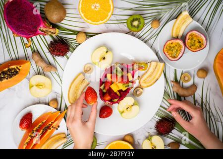 Vista dall'alto dei piatti con frutta a fette. Assortimento di diversi frutti esotici su tavolo in marmo. Colazione deliziosa, cibo sano, estate. Mano femmina h Foto Stock