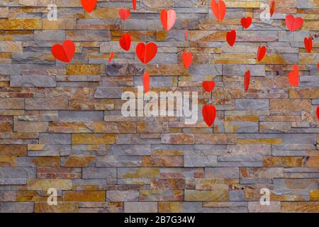 Sfondo artificiale in pietra sulla parete. Cuori rossi appesi per San Valentino. Prodotti di carta fatti in casa. Foto Stock