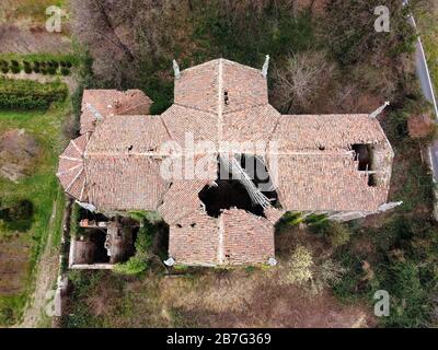 Vecchia chiesa abbandonata con tetto crollante e un buco gaping con piastrelle mancanti vista dall'alto da un drone Foto Stock