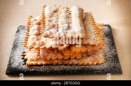 Specialità chiacchiere italiano, dolci biscotti di carnevale di pasta croccante fritta cosparsi di zucchero in polvere impilato su un vassoio in primo piano Foto Stock