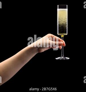 Donna mano che tiene un bicchiere di champagne frizzante isolato su nero. Foto Stock