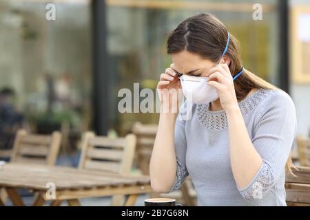 Donna seria che mette sulla maschera protettiva che impedisce il contagio alla terrazza del bar Foto Stock