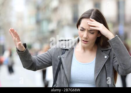 Vista frontale ritratto di una giovane donna capogiro che si sente malata su una strada della città Foto Stock