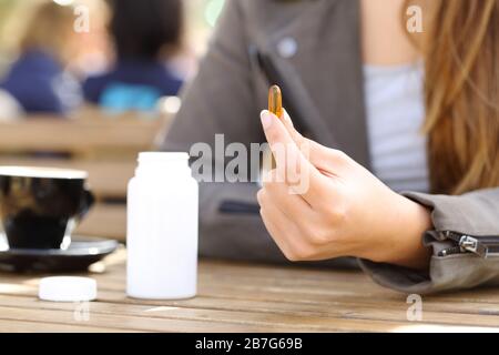 Primo piano di una mano donna che mostra supplemento pillola di vitamina su una terrazza bar Foto Stock