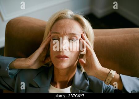 Ritratto di uomo d'affari maturo stressato strofinando templi che soffrono di mal di testa mentre si siede in sedia con gli occhi chiusi, copia spazio Foto Stock